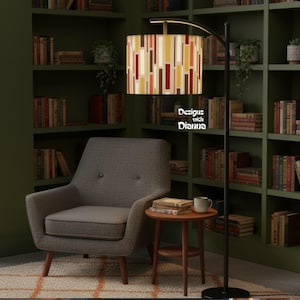 May include: A floor lamp with a patterned lampshade featuring vertical stripes in cream, yellow, red, and brown. The lamp is positioned next to a gray armchair and a small wooden side table. The text "Designs with Dianna" is visible on the lampshade.