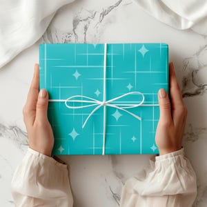 May include: A rectangular gift box wrapped in bright turquoise paper featuring a white grid pattern and scattered four-pointed star shapes. The package is tied with a thin white ribbon arranged in a simple bow centered on the front surface.
