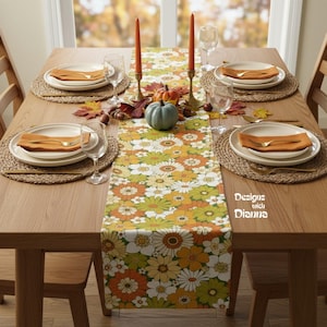 May include: A wooden dining table set for a fall meal. The table is adorned with a floral table runner, placemats, plates, napkins, and glassware. Decorative pumpkins, candles, and fall leaves complete the autumnal theme. The table setting is designed for a cozy dining experience.