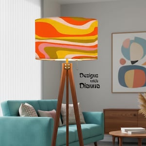 May include: A mid-century modern style floor lamp with a wooden tripod base and a colorful lampshade. The lampshade features a retro wavy pattern in orange, yellow, pink, and olive green. The text "Designs with Dianna" is visible on the side.