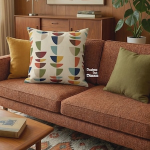 May include: A square throw pillow featuring a cream background with a repeating pattern of multicolored semi-circles in shades of blue, green, yellow, and rust. The text "Designs with Dianna" is printed in white on the center of the pillow.