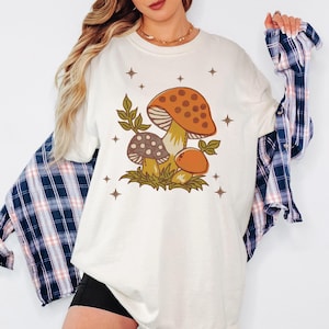 Vintage-style mushroom shirt worn with plaid, styled for fall vibes, great birthday gift for Gen Z or boho lovers 🍄