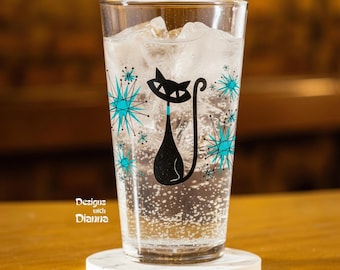 May include: A clear glass tumbler filled with ice and a carbonated beverage, featuring a black cat graphic with a teal collar and teal starburst patterns. The text "Designs with Dianna" is printed in white on the lower left side of the glass.