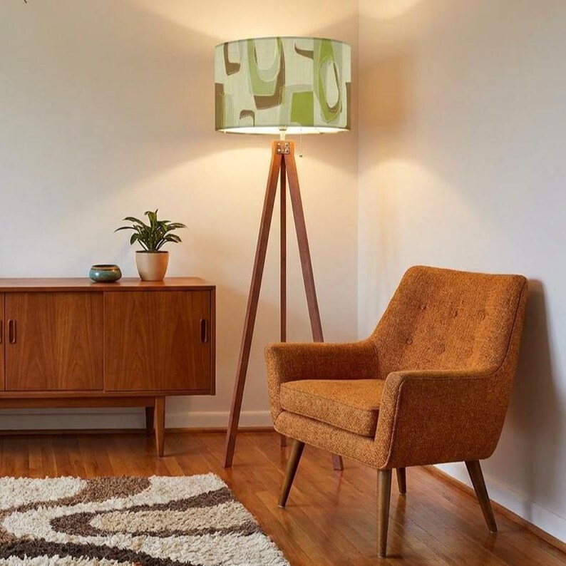 Olive green Mid Century Modern floor lamp with wooden tripod base and geometric fabric shade.
Retro floor lamp featuring a bold abstract drum lampshade inspired by 1950s Atomic design.
