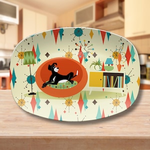 May include: A white oval serving platter with a mid-century modern design featuring a black and white dog sitting in a red egg-shaped chair. The background is a pattern of teal, red, and yellow diamonds and stars.