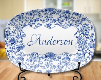 May include: White oval serving platter with a blue and white floral pattern. The platter has a white oval label with the name "Anderson" in blue cursive writing. The platter is on a black metal stand.