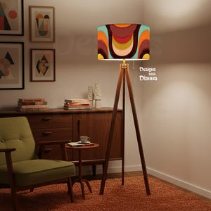 May include: A mid-century modern style floor lamp with a wooden tripod base and a colorful patterned lampshade. The lampshade features a retro design with orange, brown, and teal hues. The text "Designs with Dianna" is visible on the lampshade.