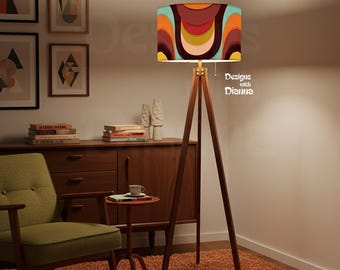 May include: A mid-century modern style floor lamp with a wooden tripod base and a colorful patterned lampshade. The lampshade features a retro design with orange, brown, and teal hues. The text "Designs with Dianna" is visible on the lampshade.
