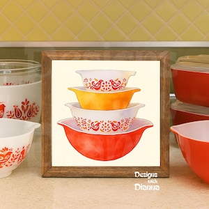 May include: A framed watercolor print featuring a stack of four vintage mixing bowls in shades of red, orange, and white. The bowls have a decorative bird and floral pattern. The frame is made of wood, and the text "Designs with Dianna" is visible.
