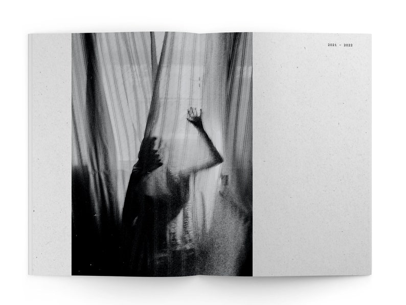 May include: A black and white photograph of a person standing behind a sheer curtain. The person's hand is raised, and their body is partially obscured by the curtain.