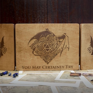 May include: Three wooden boxes with engraved designs. The center box features a dragon curled around a twenty-sided die with the text "You May Certainly Try". The boxes are made of light brown wood.