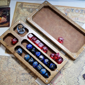 May include: A wooden dice tray with compartments for different dice sizes. The tray is open and has a variety of colorful dice inside. The tray is made of wood with a natural finish.