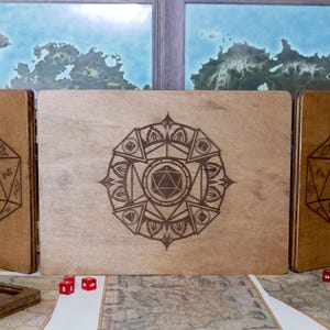 Puede incluir: Una caja de madera con tres paneles, cada uno con un diseño grabado diferente. El panel central tiene un diseño tipo mandala con un dado D20 en el centro. Los paneles izquierdo y derecho tienen un dado D20 grabado. La caja está sentada en una mesa con dados esparcidos alrededor.