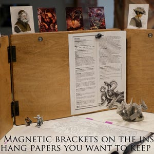 May include: A wooden tabletop gaming screen with magnetic brackets on the inside to hold papers. The screen is folded open to reveal a printed sheet of paper with the word "Heroes" at the top. There are also several small images attached to the screen with magnets.