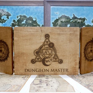 May include: A three-panel wooden Dungeon Master screen with a laser-etched design of a crescent moon, a five-pointed star, and a 20-sided die inside a triangle. The center panel reads "Dungeon Master".