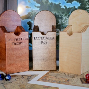 Puede incluir: Tres cajas de dados de madera con diferentes manchas de madera. Las cajas tienen una ranura en la parte superior para que los dados se puedan tirar. Las cajas est&aacute;n grabadas con las frases "Let the Dice Decide", "Iacta Alea Est" y una caja en blanco.
