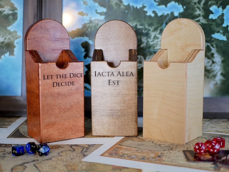 Puede incluir: Tres cajas de dados de madera con diferentes manchas de madera. Las cajas tienen una ranura en la parte superior para que los dados se puedan tirar. Las cajas est&aacute;n grabadas con las frases "Let the Dice Decide", "Iacta Alea Est" y una caja en blanco.