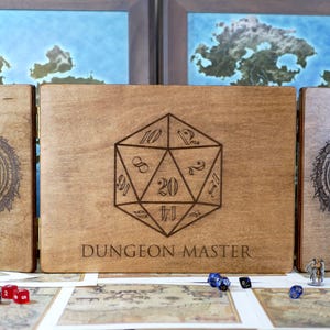 May include: A wooden box with three panels, each featuring a different design. The center panel has a large, engraved image of a twenty-sided die with the text "DUNGEON MASTER". The left and right panels have engraved images of a circle with a five-pointed star inside.