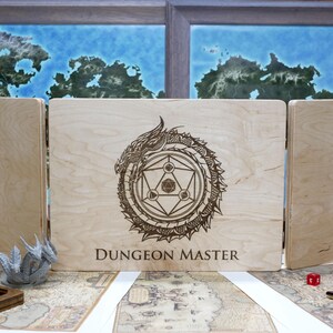 May include: A wooden box with three panels, each with a different design. The center panel features a dragon design with the words "Dungeon Master" engraved below. The box is made of light wood and has a natural finish.