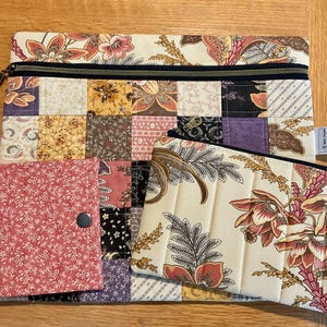May include: A quilted patchwork laptop sleeve with a black zipper, a small matching pouch, and a small wallet. The sleeve and pouch feature a floral pattern on a cream background. The wallet is a small, red floral print.
