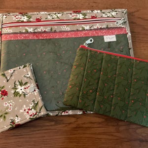 May include: A collection of fabric pouches and a wallet. The large pouch features a floral pattern with red and white flowers on a beige background. The smaller pouch is olive green with a red zip and a quilted design. The wallet has a floral pattern.
