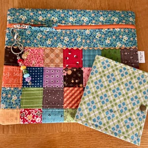 May include: A rectangular zipped pouch featuring a teal floral top section and a multi-coloured patchwork body with a beaded keychain attached. Beside it sits a smaller square folding pouch with a green and blue plaid pattern and a metal snap.