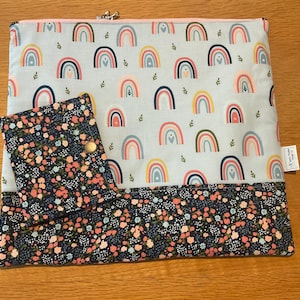 May include: A light blue fabric case and matching wallet with a rainbow pattern. The case has a zip closure and a floral patterned bottom border. The wallet has a snap closure and a floral pattern.