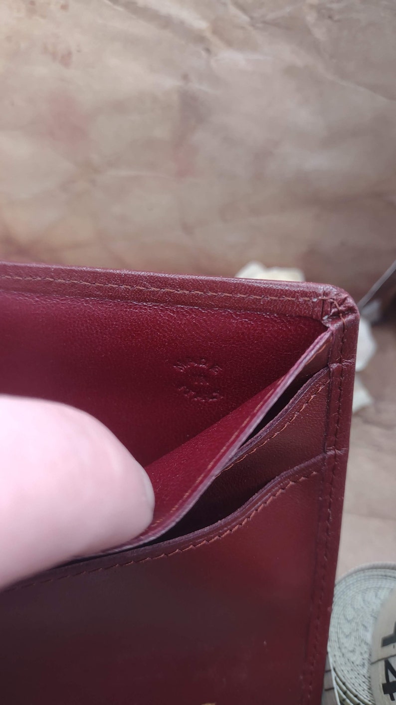 May include: The inside of a burgundy leather wallet with the text "Cartier Paris" embossed in gold.