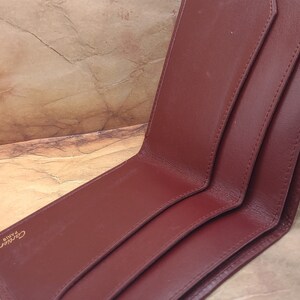 May include: A burgundy leather wallet with gold accents and the text "Cartier Paris" embossed on the front.
