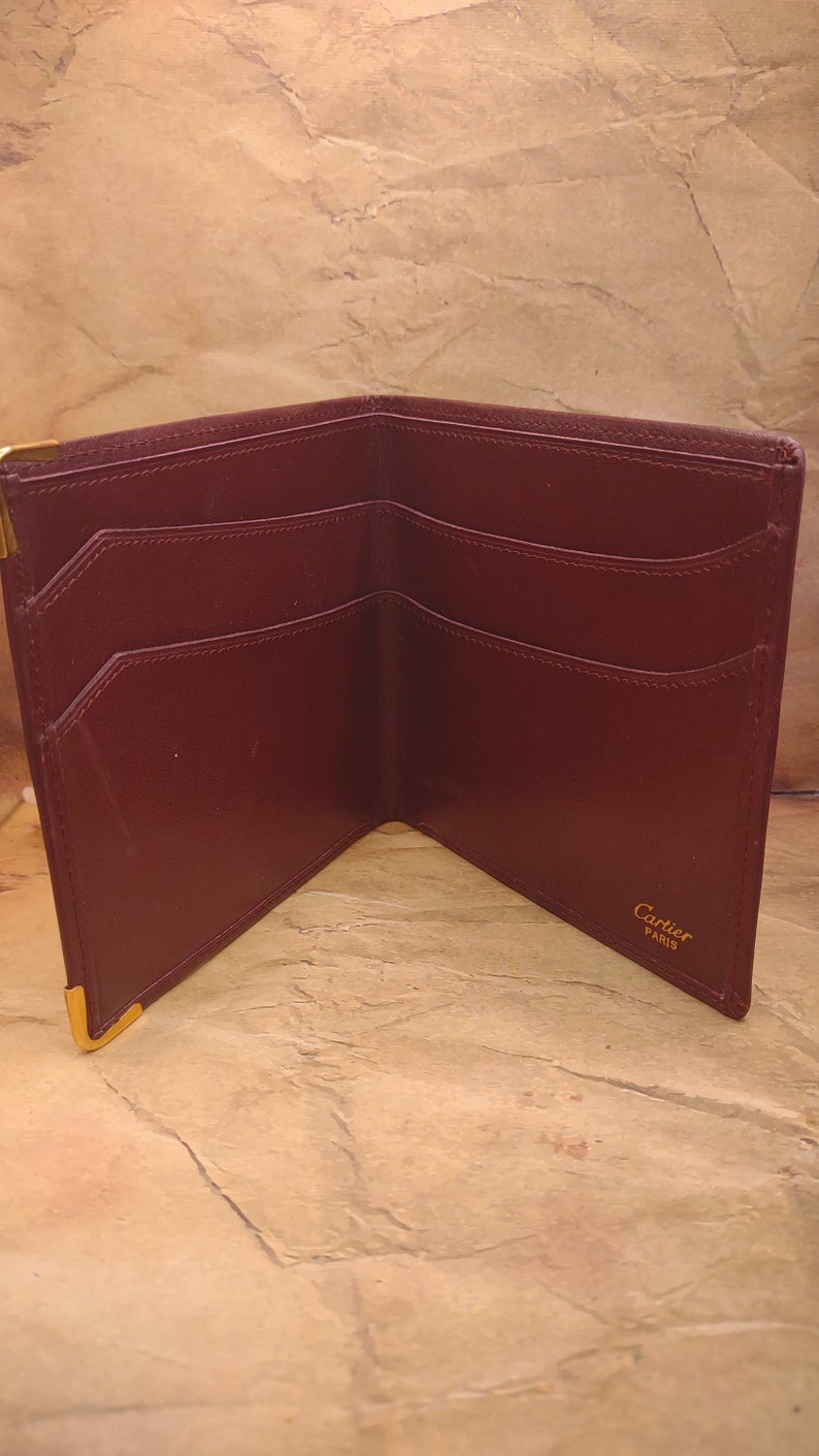 May include: A burgundy leather wallet with gold accents and the text "Cartier Paris" on the inside.