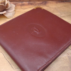 May include: A burgundy leather wallet with a gold embossed Cartier logo.