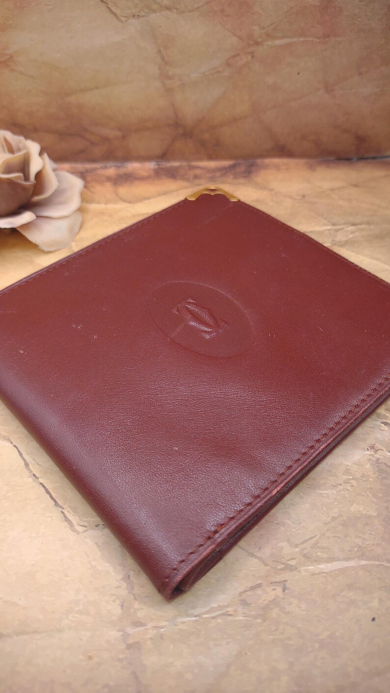 May include: A burgundy leather wallet with a gold embossed Cartier logo.