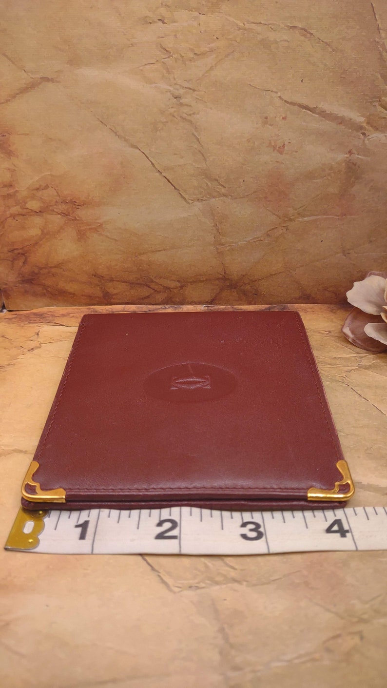 May include: A burgundy leather wallet with gold accents and a gold embossed logo. The wallet is approximately 3 inches wide.