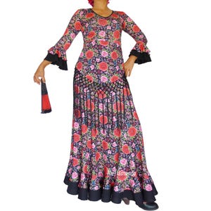 May include: A long-sleeved, floral-print dress with a black trim and a ruffled hem. The dress features a V-neckline and bell sleeves with black ruffles. A matching fan is held in the hand. The dress is adorned with red roses and other flowers.
