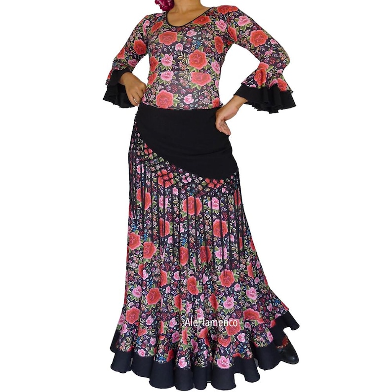 May include: A flamenco dress with a floral print top and a long skirt. The top has long sleeves with black frilled cuffs. The skirt is black with a floral design in red, pink, and green. The outfit is designed for flamenco dancing.