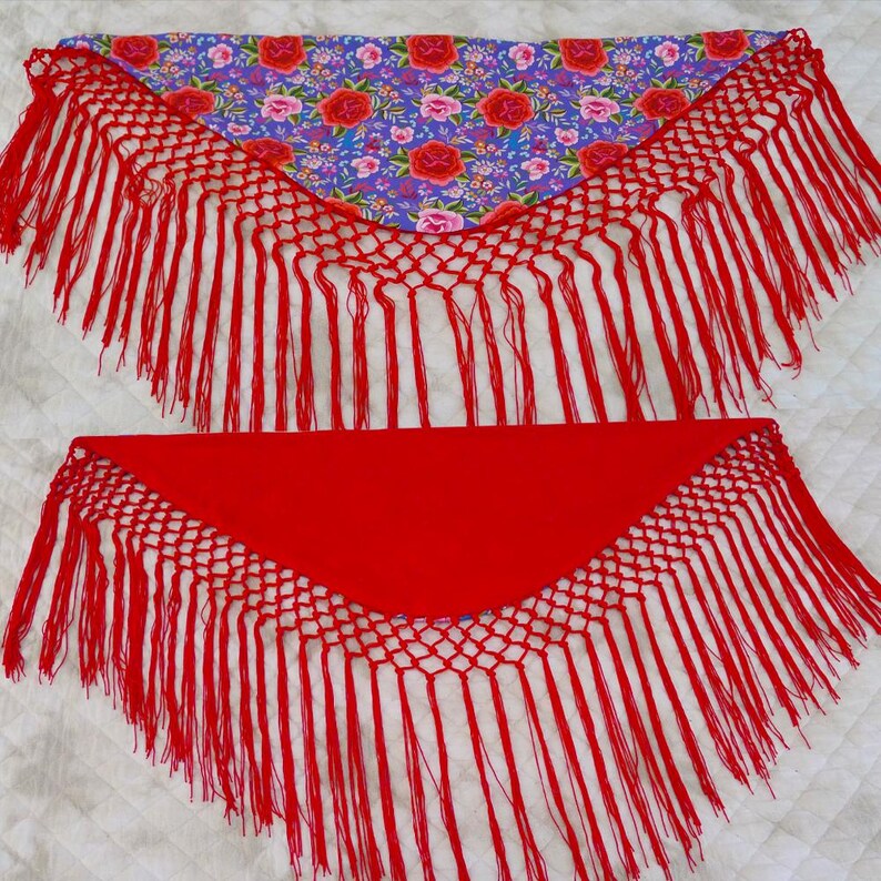 May include: Two triangular shawls. One has a red fringe and a floral pattern on a purple background. The other is solid red with a red fringe. The shawls are likely for dance or costume.