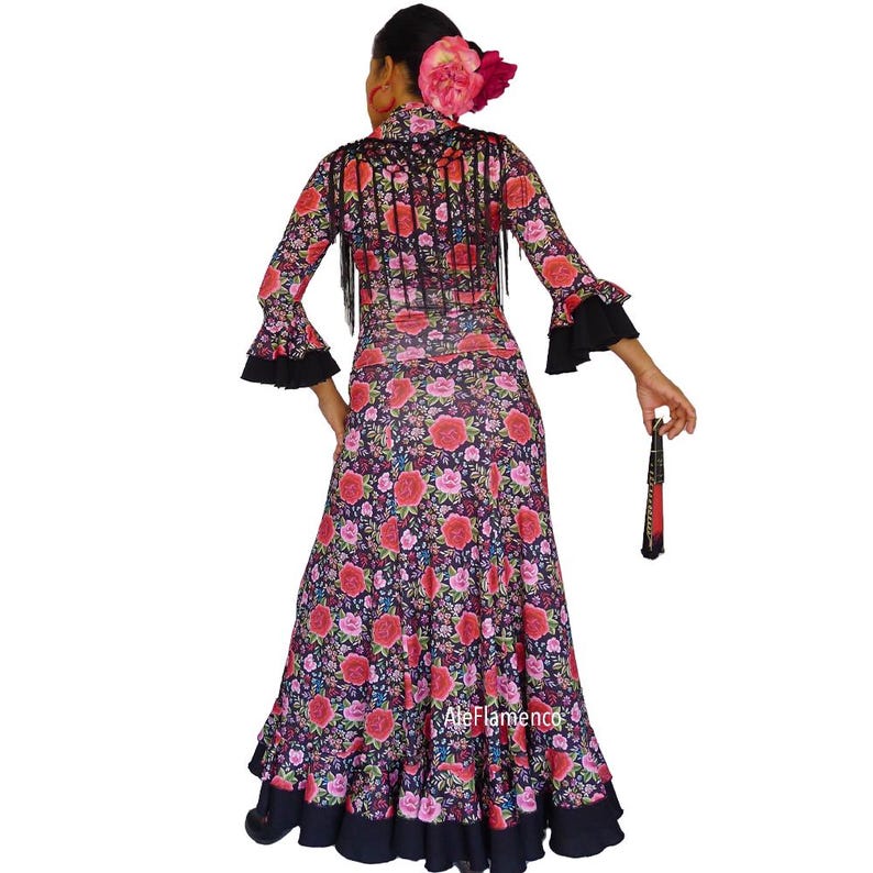 May include: A long-sleeved flamenco dress with a floral pattern of red and pink roses on a dark background. The dress has black fringe and accents, with a matching fan. The dress is designed for dance performances.