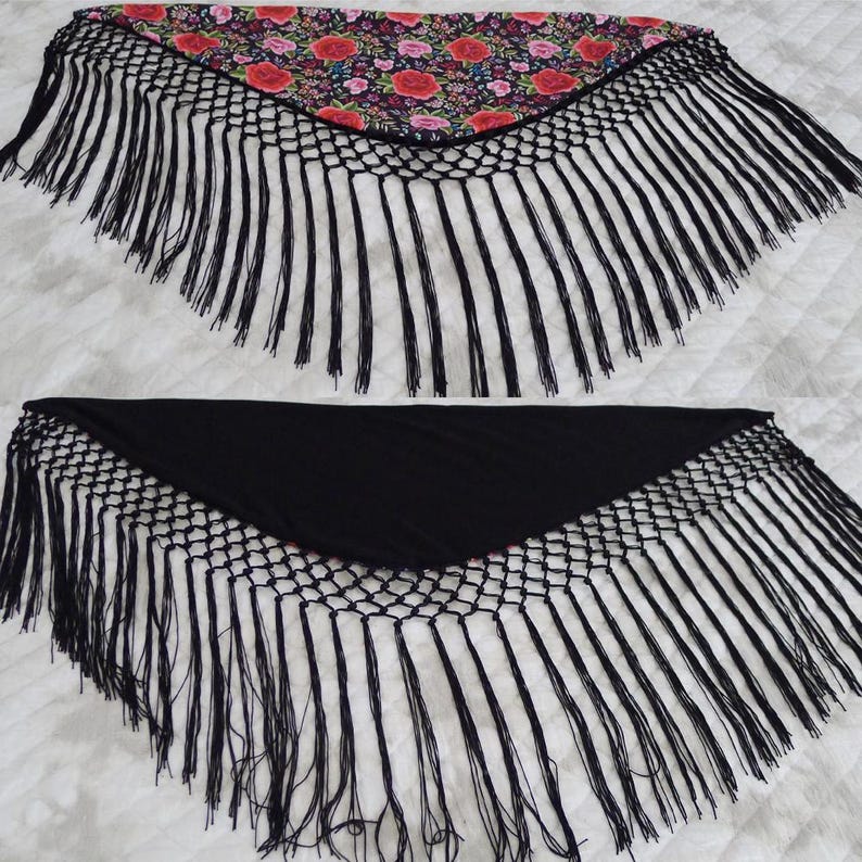 May include: Two triangular shawls. One has a floral pattern with red roses on a black base, the other is plain black. Both have long, black fringe along the edges, creating a decorative and elegant appearance.
