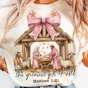 The Greatest Gift of All text design with a nativity scene illustration and pink bow