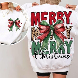 Puede incluir: Sudadera blanca con un diseño de estampado de leopardo, verde y rojo que dice "Merry Merry Christmas" con un gran lazo rojo en el centro.
