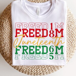May include: White t-shirt with the words "FREEDOM" in red, "Juneteenth" in gold, and "FREEDOM" in green.