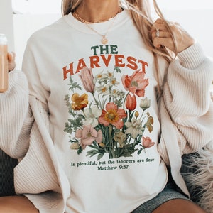 May include: A white sweatshirt with a floral design and the text "THE HARVEST is plentiful, but the laborers are few Matthew 9:37".