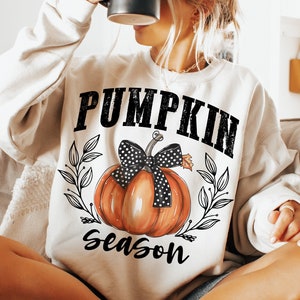 May include: A white sweatshirt with the text "Pumpkin Season" in black lettering. A cartoon pumpkin with a black and white polka dot bow is centered on the sweatshirt.