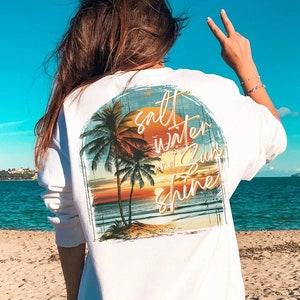 May include: White sweatshirt with a graphic print of a sunset and palm trees. The text "salt water sun shine" is printed on the graphic.
