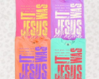 May include: Four folded t-shirts in pink, purple, orange, and teal. Each shirt features the text "IT WAS JESUS all along" in a distressed font. The shirts also have a list of words: faith, grace, truth, saved, amen, love, holy, peace, spirit.