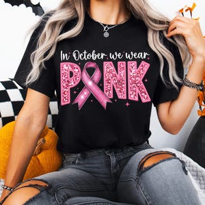 May include: A black t-shirt with a pink glitter design that says "In October we wear PINK" with a pink ribbon in the middle.