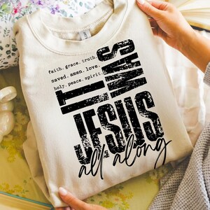 May include: A beige sweatshirt with the text "It Was Jesus All Along" in a distressed black font. The sweatshirt also features the words "faith, grace, truth, saved, amen, love, holy, peace, spirit" in a smaller font.