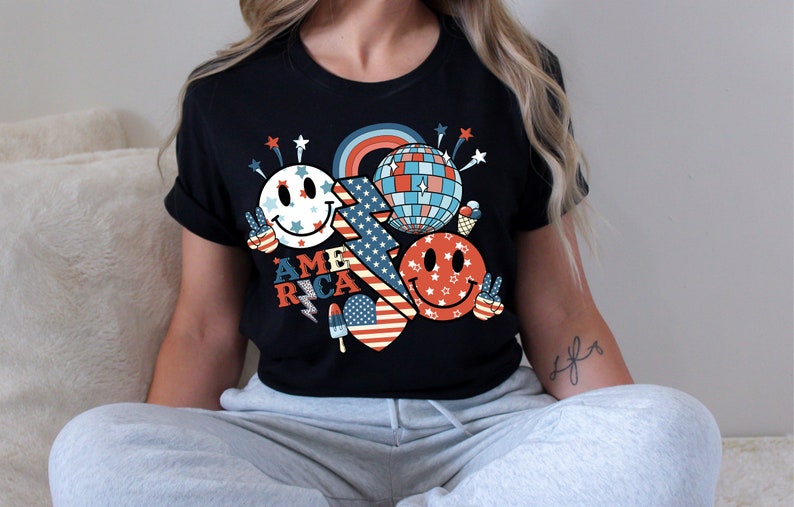 May include: Black t-shirt with a red, white and blue graphic design featuring a smiley face, a disco ball, fireworks, and the word "AMERICA".