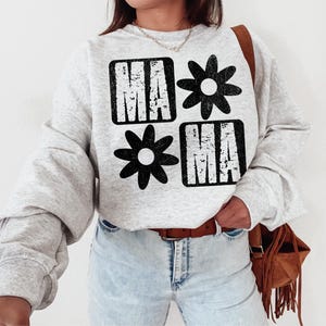 Peut inclure: Un sweat-shirt gris avec un motif graphique noir qui dit "Mama" avec un motif de fleur entre les mots.