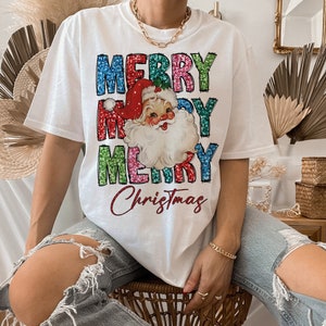 Op de afbeelding: Wit T-shirt met een kleurrijke, glinsterende "Merry Christmas"-afbeelding met een vintage illustratie van de kerstman.